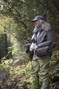 A woman holding a fly rod in the woods.