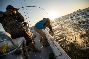 Two men are fishing on a boat at sunset.