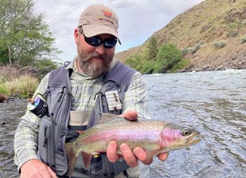 A man holding a rainbow trout in a river.