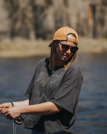 A woman wearing sunglasses and a hat is holding a fishing rod.