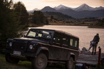 A land rover parked next to a lake with mountains in the background.