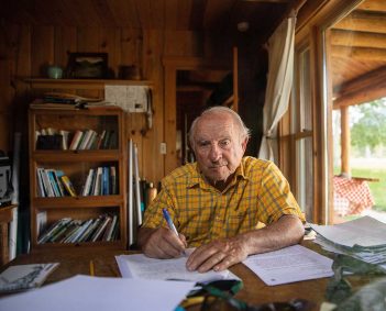 An older man sitting at a desk in a cabin.