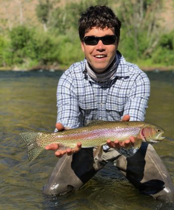 A man holding a rainbow trout in a river.