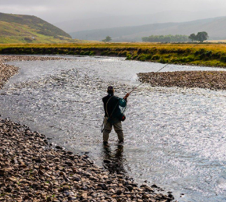 A man is fly fishing in a river in scotland.