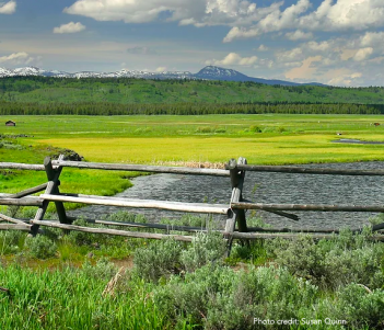 A wooden fence in the middle of a grassy field with mountains in the background.