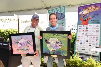 Two people holding up framed paintings at an event.
