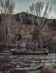 Two men fishing in an inflatable boat on a river.