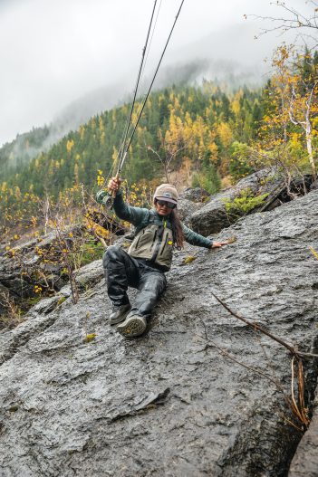 A woman holding a fly rod on a rock.