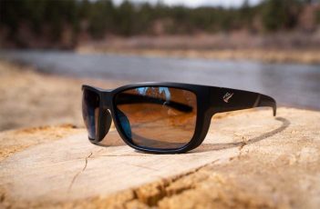 A pair of sunglasses sitting on a log next to a river.