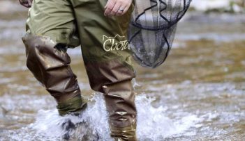 A man wading through a river in waders.