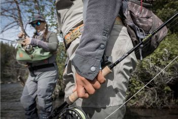 Two people are standing on a river holding their fishing rods.