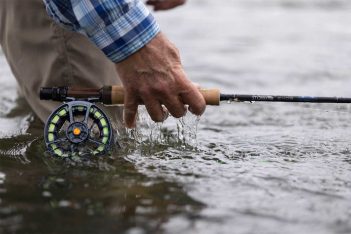 A person holding a fly fishing reel in the water.