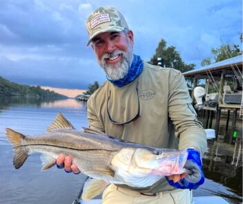 A man holding up a striped bass on a boat.