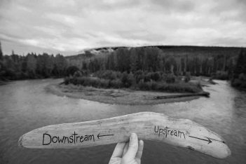 A person holding a wooden stick with the word downstream written on it.