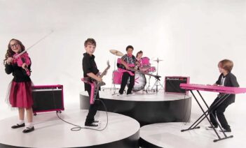 A group of children playing instruments in front of a pink background.