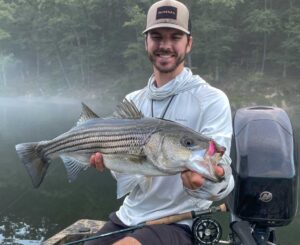 A man holding a striped bass on a boat.