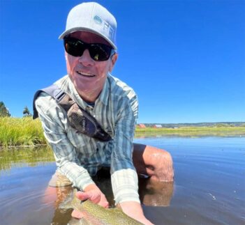 Patrick Berry holding a rainbow trout in the water.