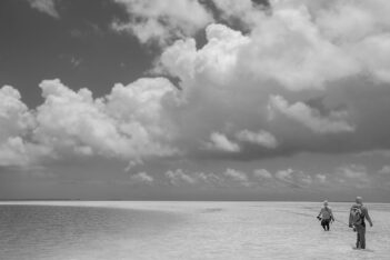 Two people walking on the beach in black and white.