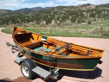 A wooden boat on a trailer with mountains in the background.