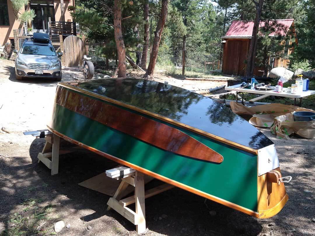 A green and brown boat is sitting on a trailer.