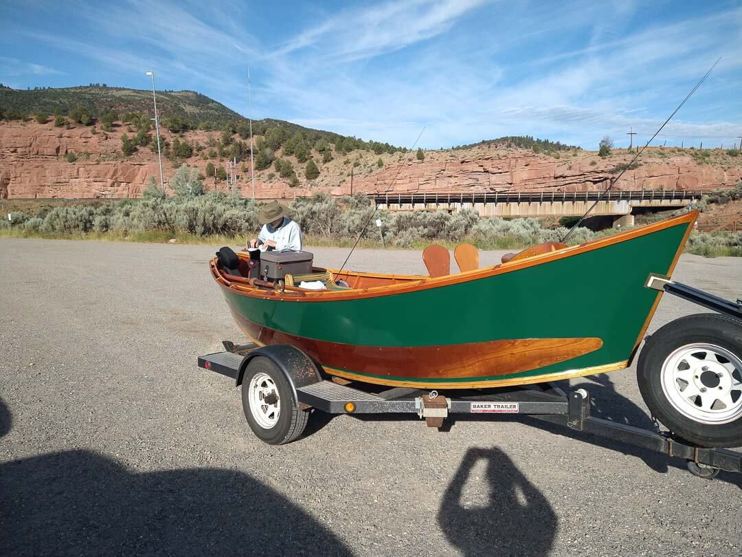 A green and brown boat on a trailer.
