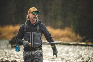 Man fly fishing in the rain while wearing sunglasses and a cap.