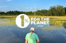 A person standing on a paddleboard in a marshy water area, facing away, with logos indicating membership in "1% for the planet" and "sustainable angler.