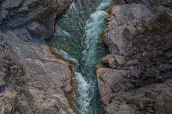 Aerial view of a narrow, fast-flowing river cutting through large gray rock formations.