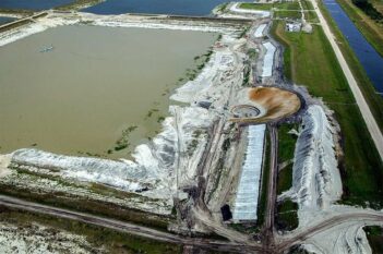 Aerial view of an industrial site with large ponds, a circular excavation area, surrounding mounds of earth, roads, and construction activity.